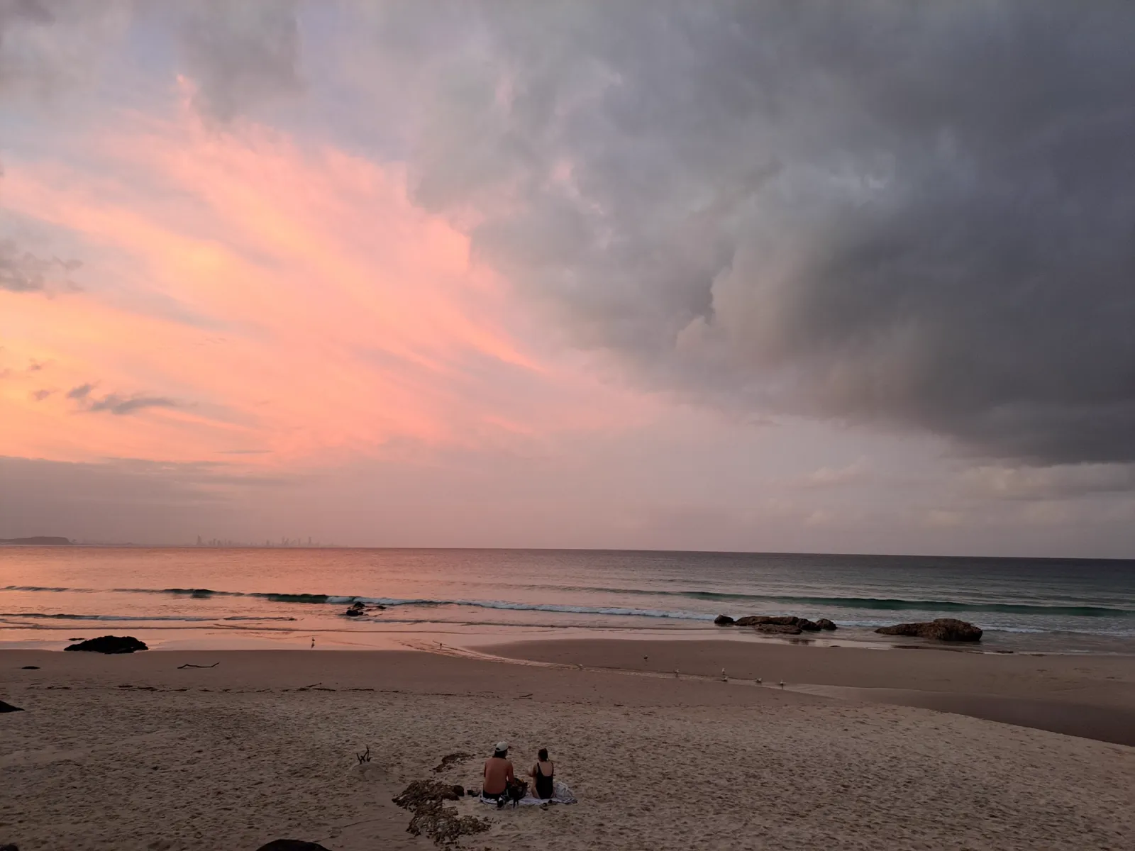 Soft pink dusk on the beach, people in the last light