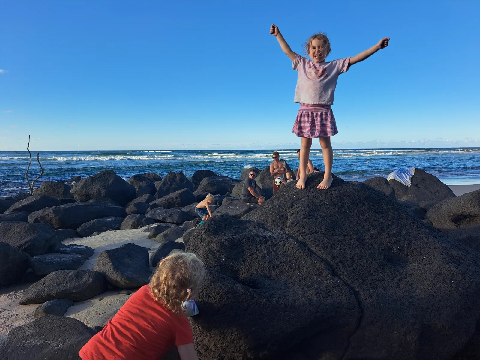 A child on the black rocks, arms spread wide
